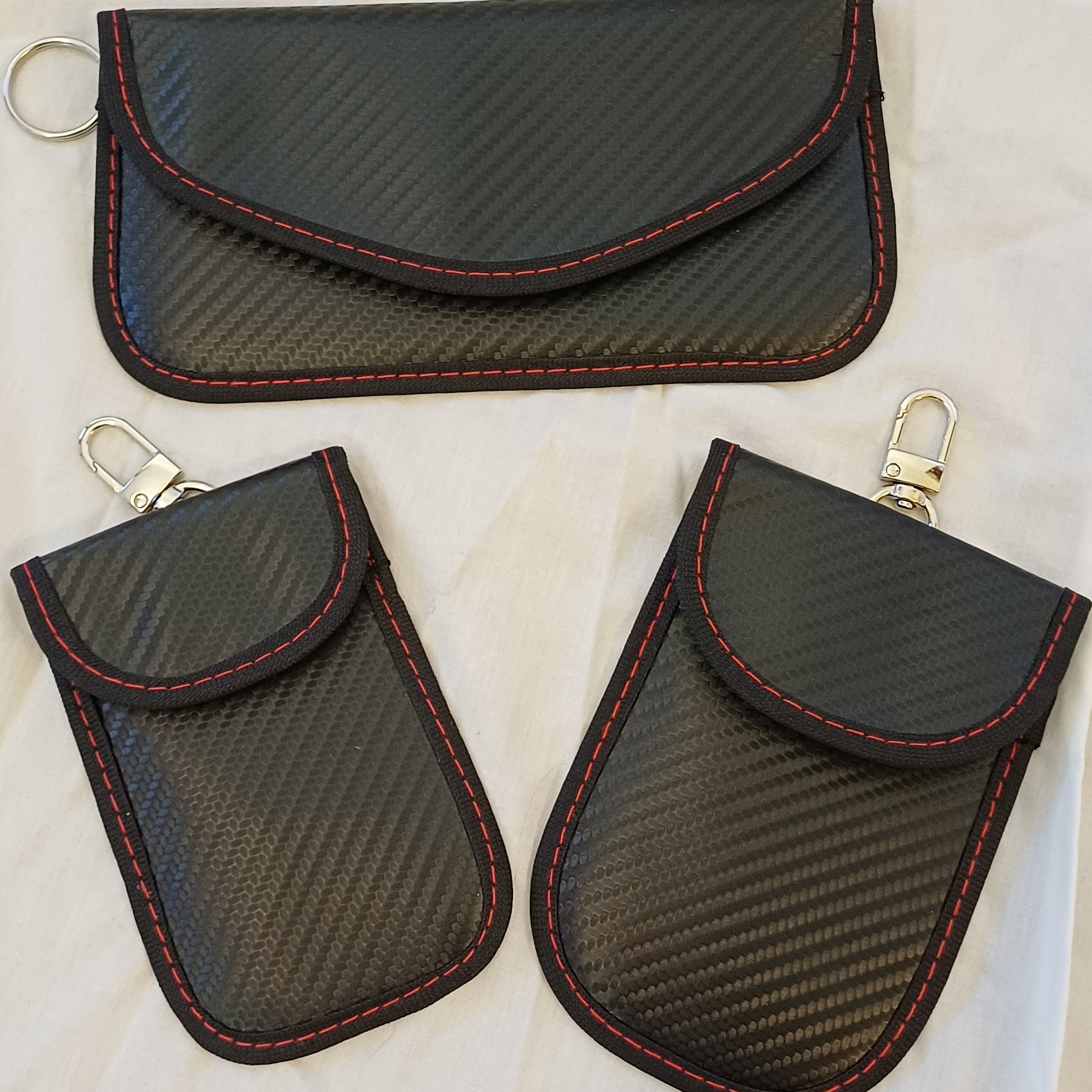 Three black carbon fiber-style key pouches with red stitching on a light background