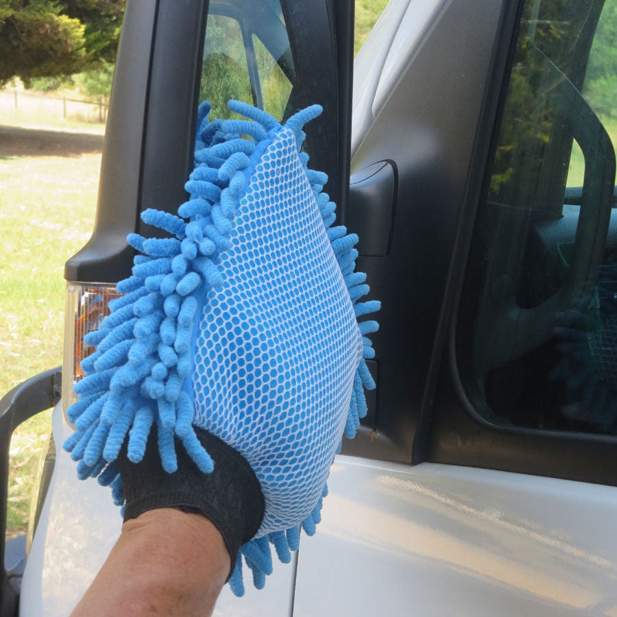 Blue microfiber cleaning glove cleaning a car mirror outdoors.