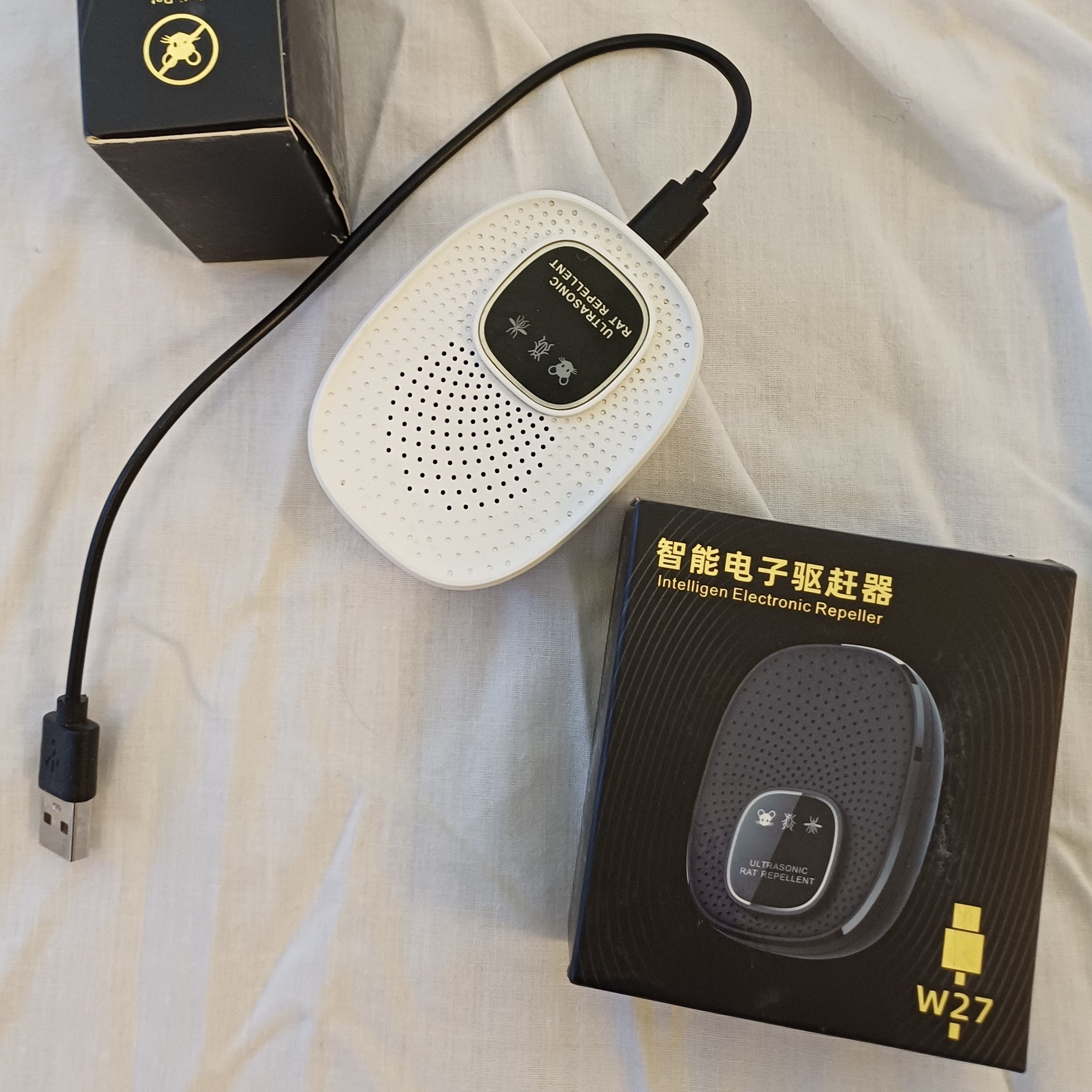 White electronic device with USB cable and black packaging on a white fabric background