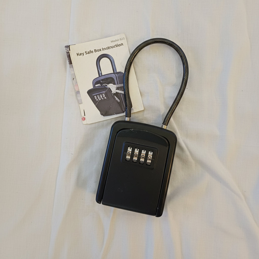 Black key safe box with combination lock and instruction manual on a beige surface
