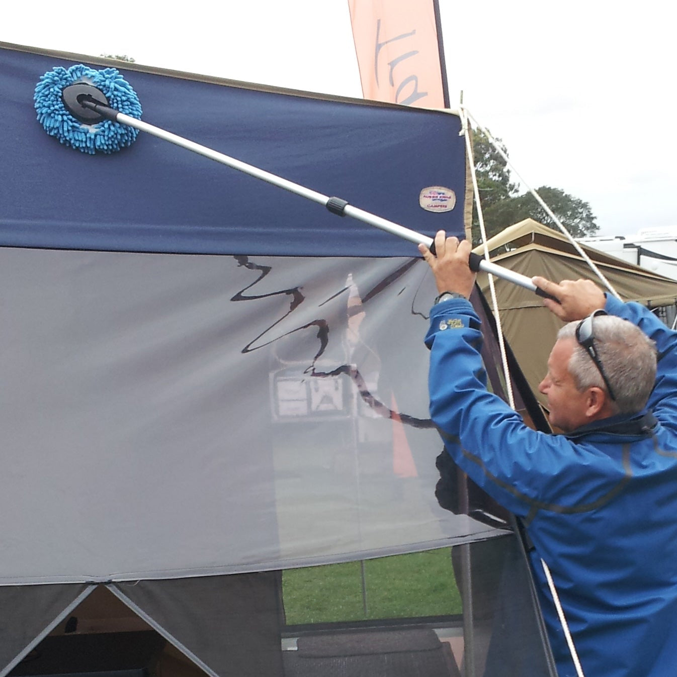 Person cleaning a tent with a brush and water, standing outside a tent. Using a Filko Cleaning Mop
