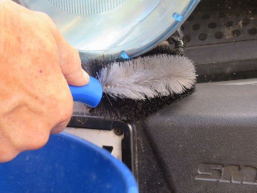 Person cleaning a car's windshield with a brush and blue bucket
